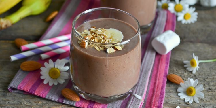 Photo of chocolate almond oatmeal smoothie in a glass with nut chips on top