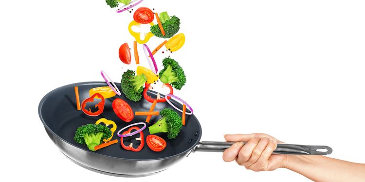 Falling vegetables in frying pan on an isolated white background